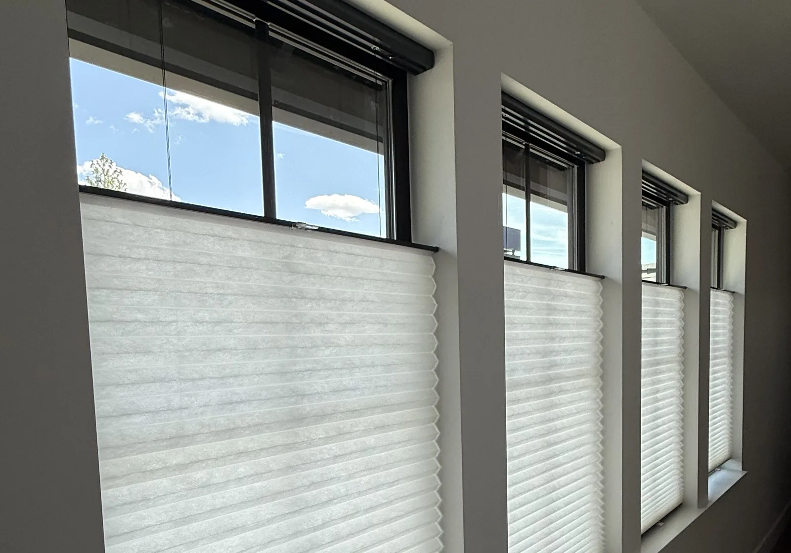 A run of windows with light-filtering cellular shades raised partway, blue sky above them