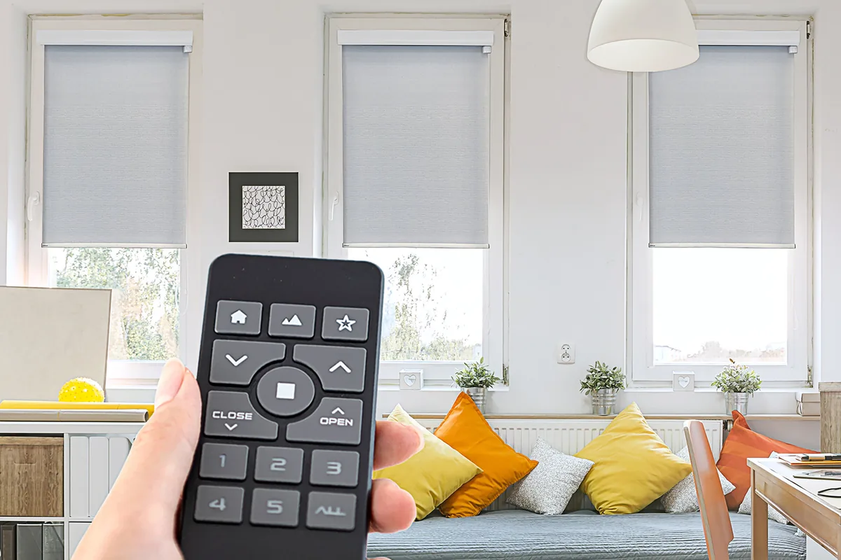A handheld remote raising a row of roller shades in a bright living room