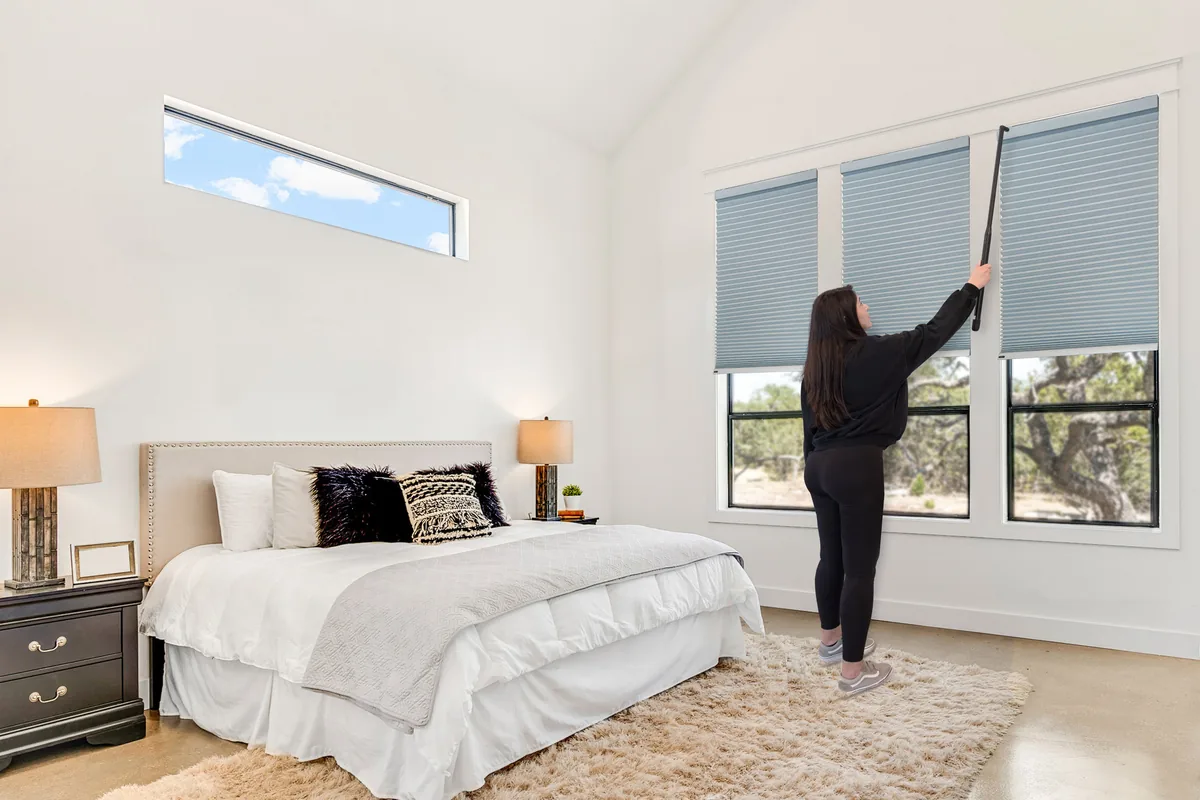 Recharging a motorized cellular shade with the lithium wand, reaching a high bedroom window
