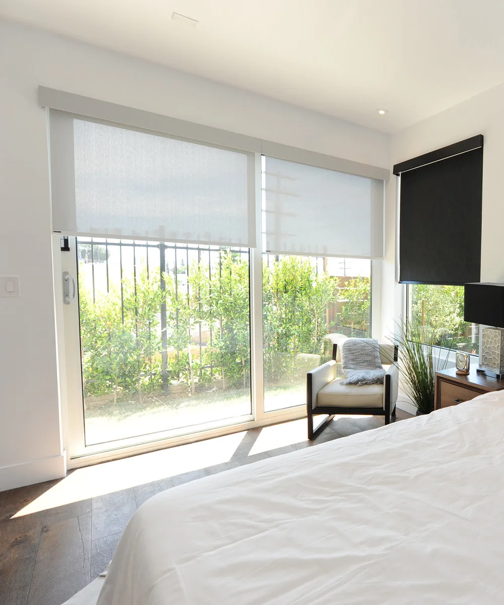 Solar roller shade lowered over a patio slider, the garden still visible through the fabric