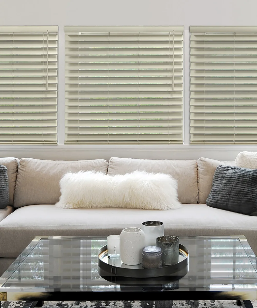 Wood blinds with decorative cloth tapes, slats tilted partly open above a sofa